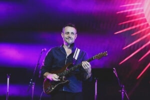 Ben Hauptmann plays the guitar under purple and pink stage lights