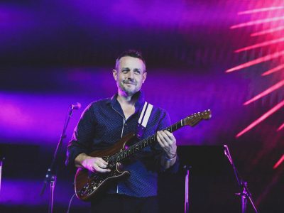 Ben Hauptmann plays the guitar under purple and pink stage lights