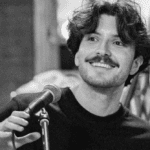 man smiles while holding a microphone and sitting at piano in black and white photograph