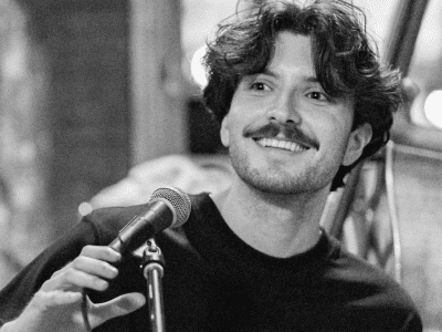man smiles while holding a microphone and sitting at piano in black and white photograph